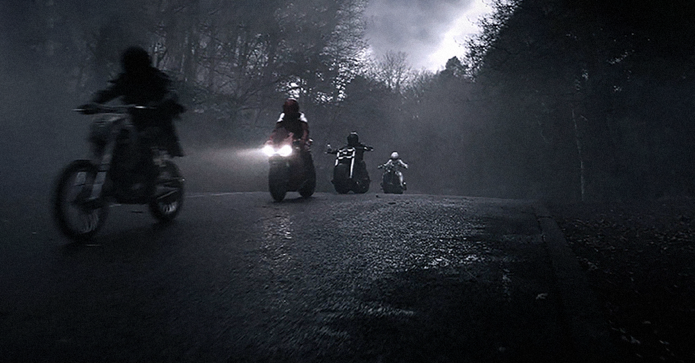 four people on motorcycles on a rainy grey street